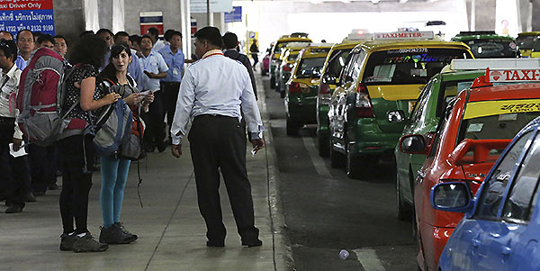 In this photo taken June 19, 2014, tourists, front left, talk to each other in front of a group of taxi drivers at a taxi stand at Suvarnabhumi international airport in Bangkok, Thailand. Since staging a coup on May 22, the military has led a crackdown on crime as part of what army commander Gen. Prayuth Chan-ocha describes as a morality cleanse for Thai society. Before democracy can be restored, he says, corruption and lawlessness have to stop. (AP Photo/Apichart Weerawong)